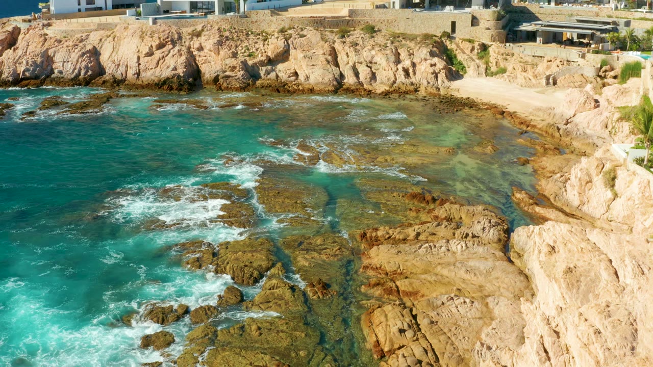 White foam spreading across shallow rock shelves beside a sandy cove.