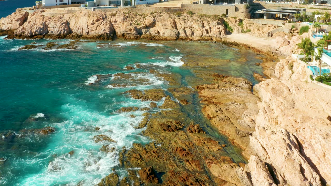 White surf spreads across brown rock shelves beside a small coastal cove.
