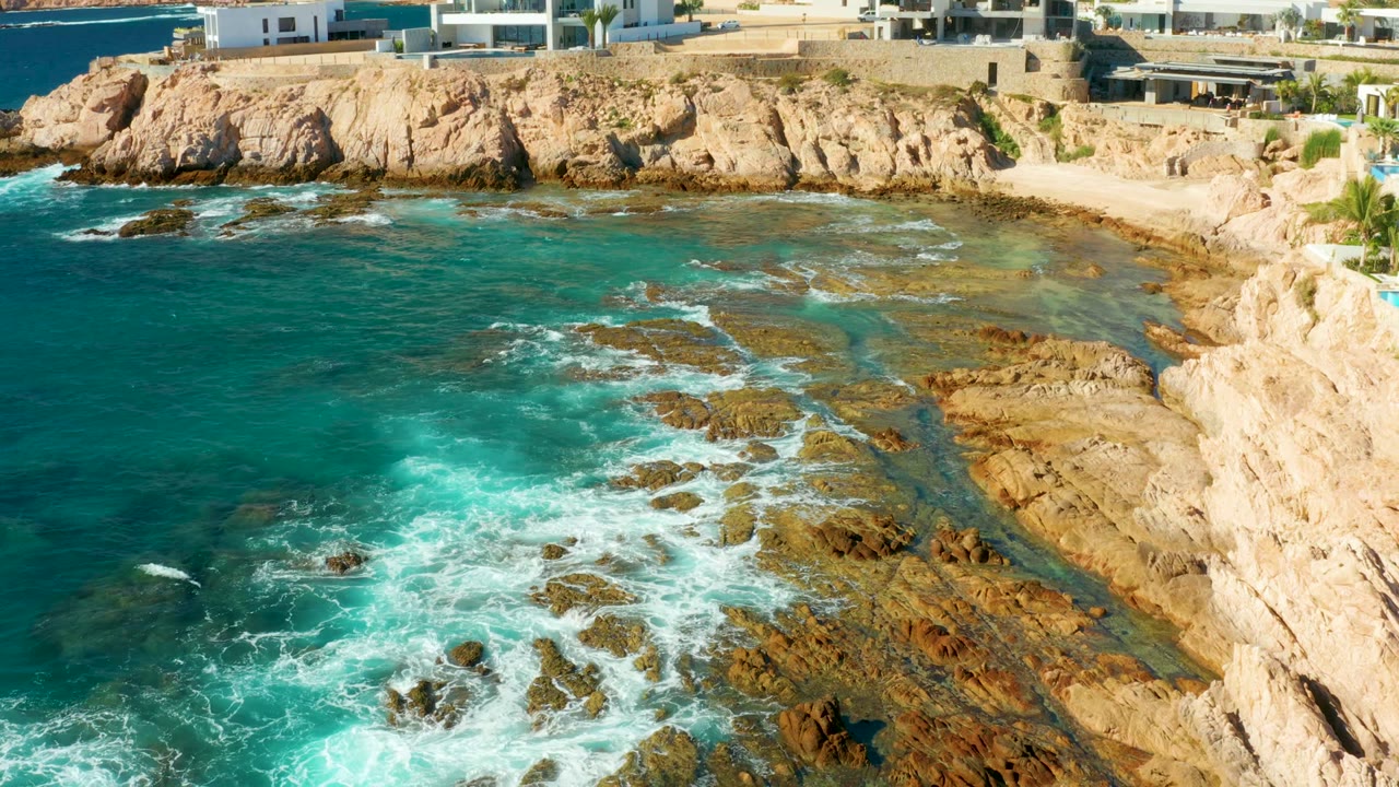 White surf spreads across exposed rocks beside a small beach cove.