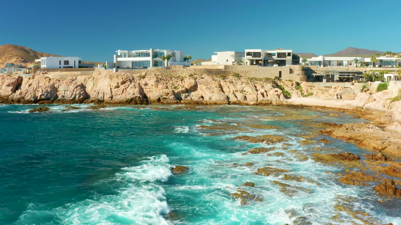 Foamy surf crossing rocks below modern cliffside buildings