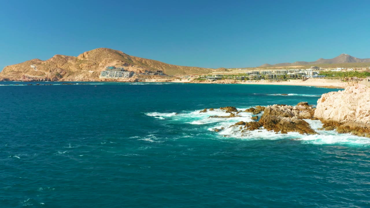 Waves foaming around rocky outcrops near a distant resort beach.