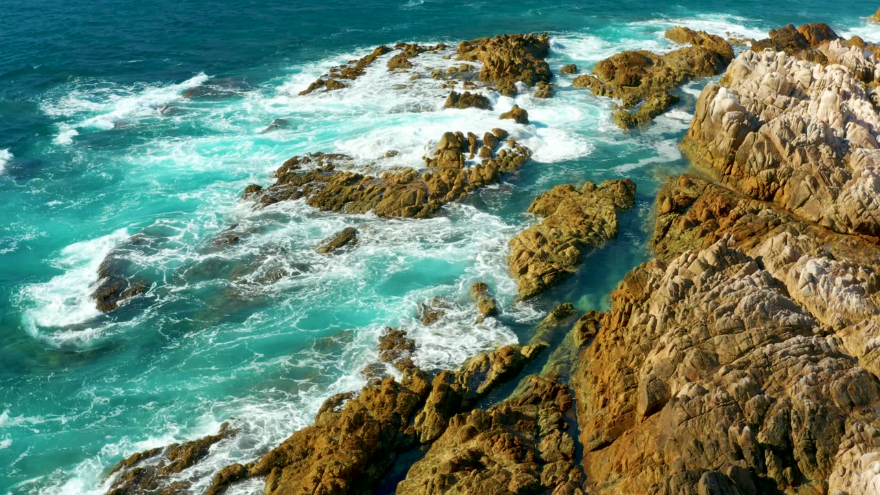 White surf swirls through rocky channels beside a pale cliff edge.