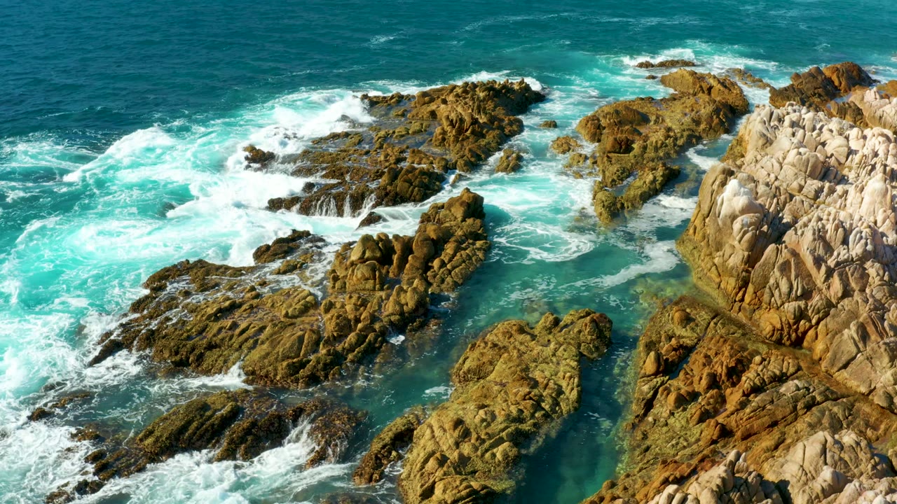 White foam spreads between rocky outcrops in turquoise water.