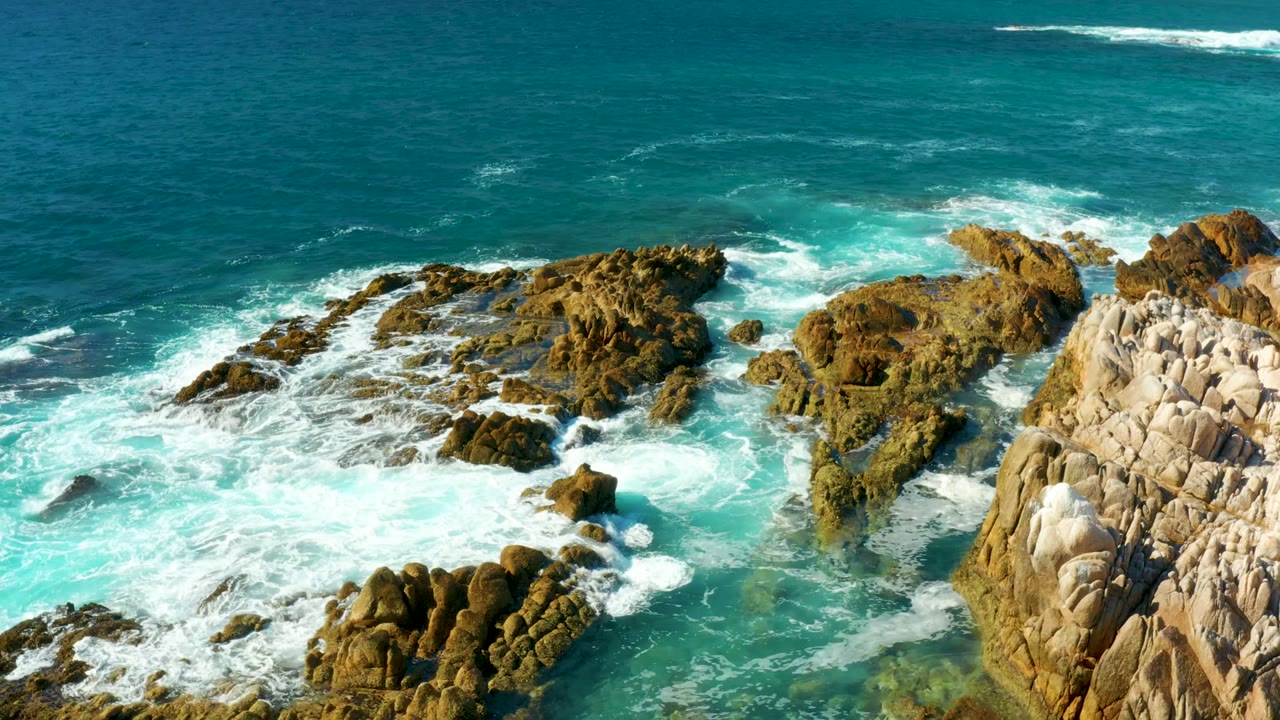 White surf spreading across jagged shoreline rocks.