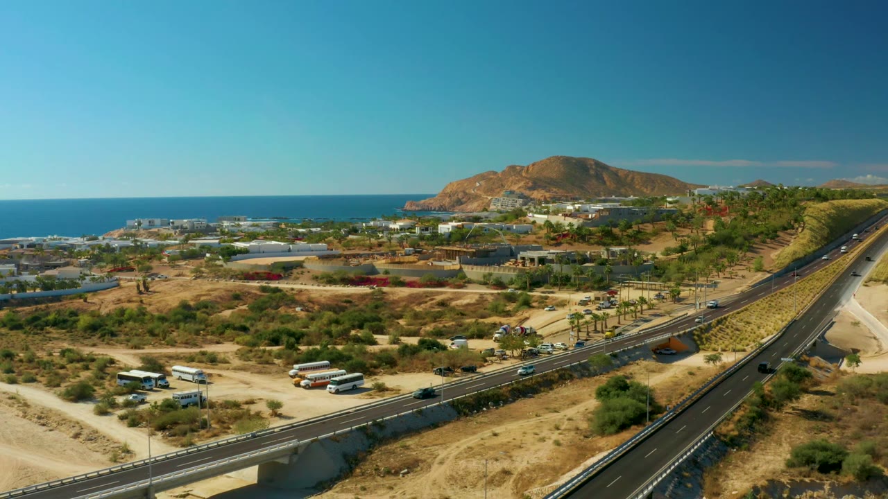 Aerial view of coastal highway traffic, dry hills, ocean, and brown ridge.