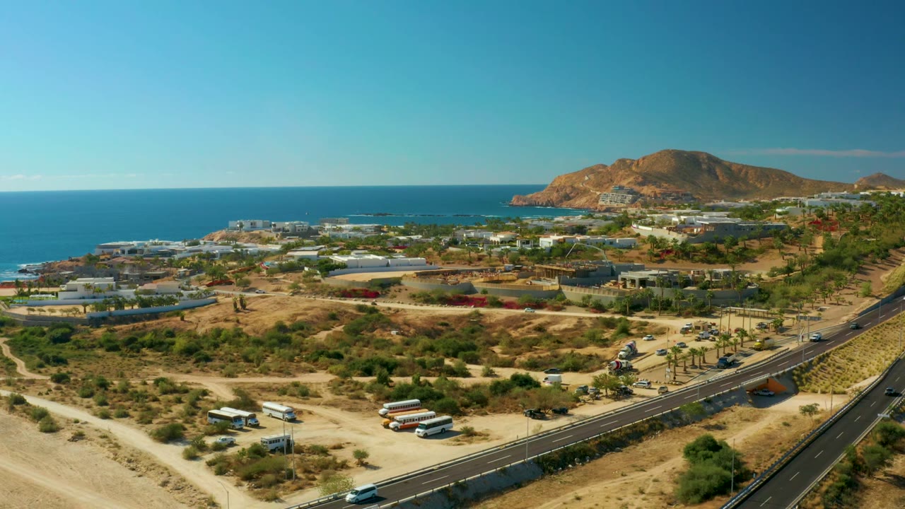 Elevated coastal highway view with ocean, hills, buildings, and vehicles.