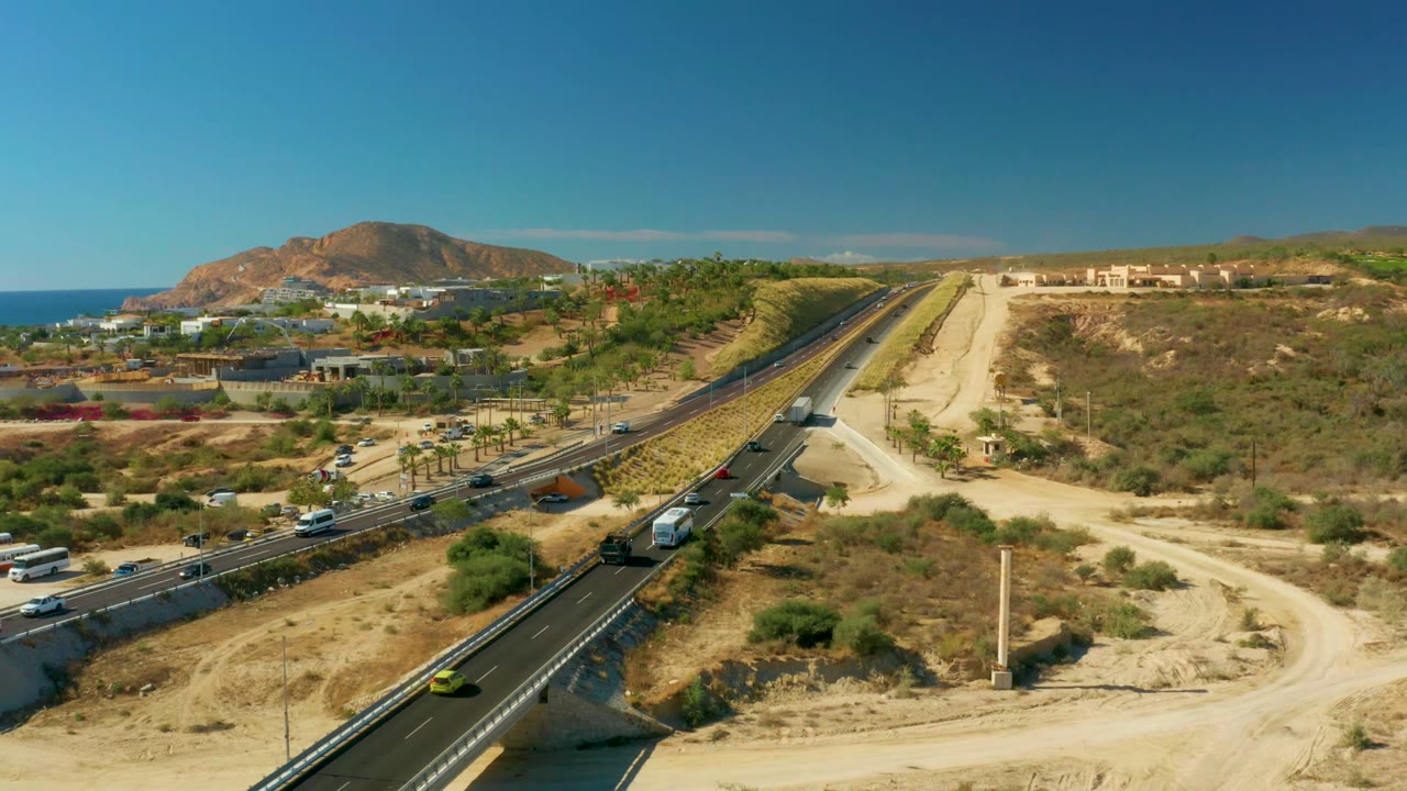 Aerial highway traffic through dry coastal hills with ocean in the distance.