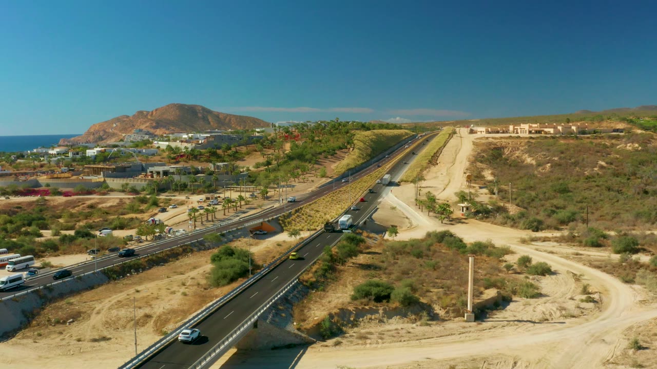 Aerial view of highway traffic with desert slopes, ocean, and mountain background.