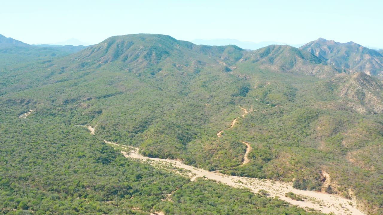 A wide aerial frame in El Salado Viejo Los Cabos with a pale wash cutting through the valley, green brush on the hillsides, and no visible people.