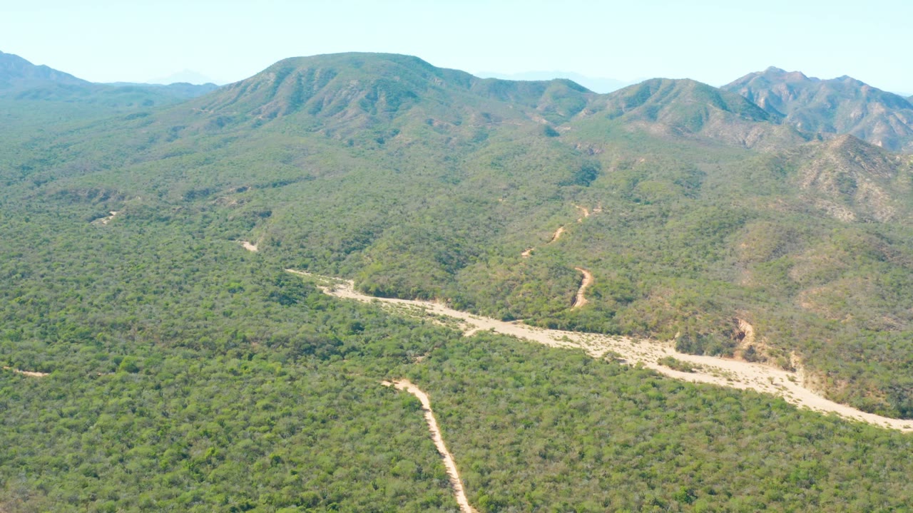 Wide aerial landscape with a pale road cutting through forested hills.