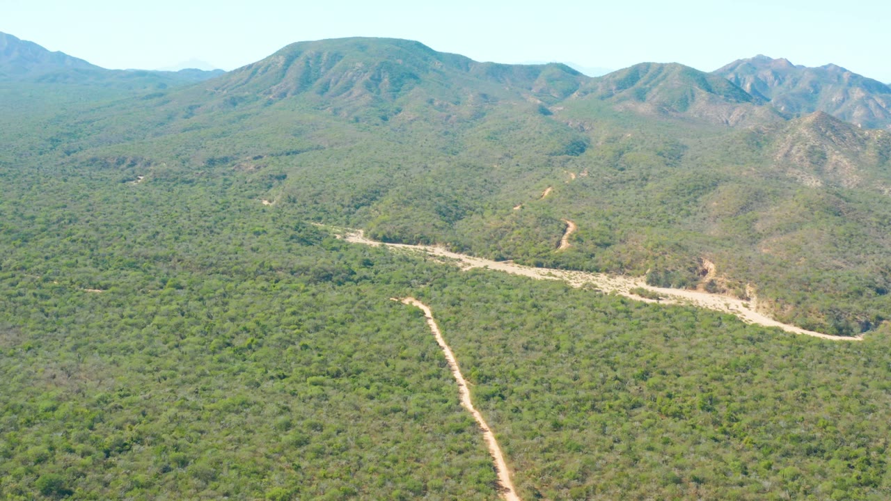 Wide aerial landscape with a dirt road and mountain ridges.