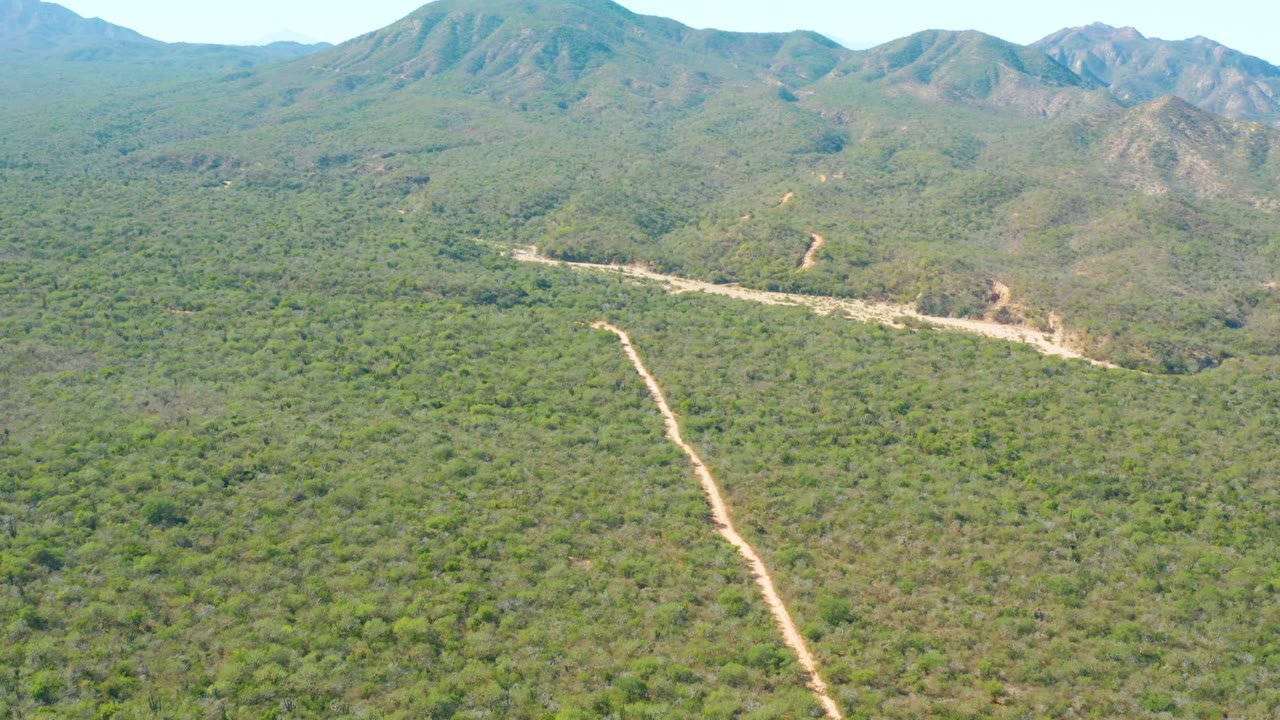 Wide aerial view of green hills, dirt roads, and mountains.