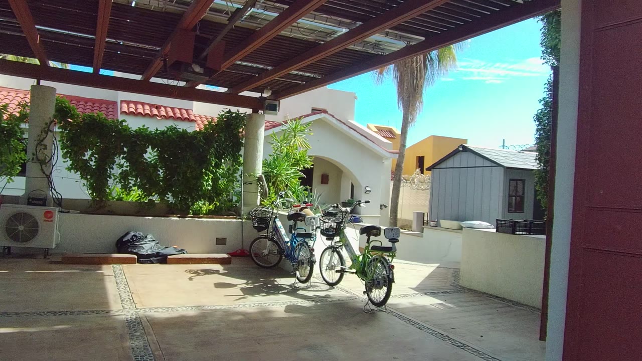 East Cape Los Cabos patio view with bicycles near the right side, vines along a white planter wall, a small light-colored outbuilding in the background, and no visible people.