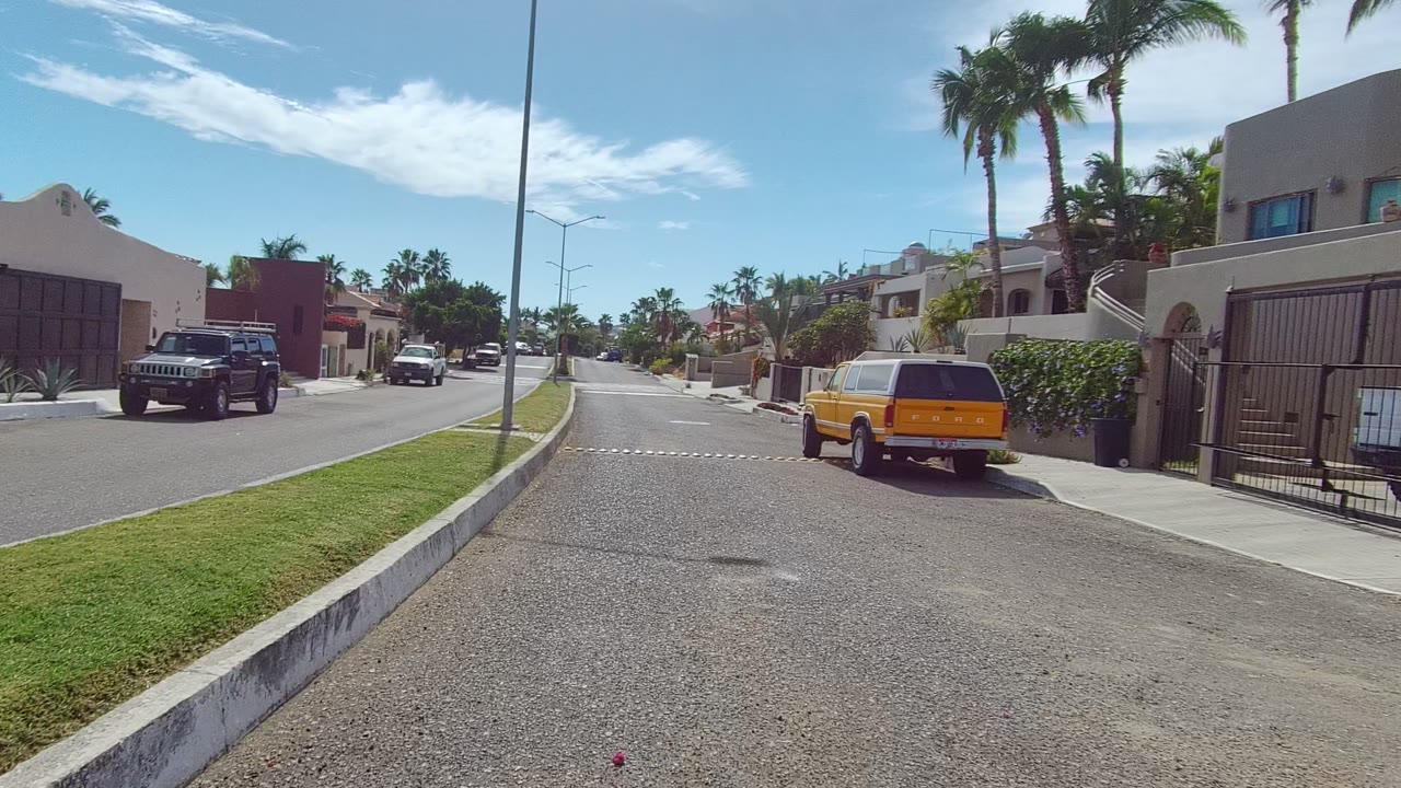 Yellow SUV beside a gated house on a sunny residential street.