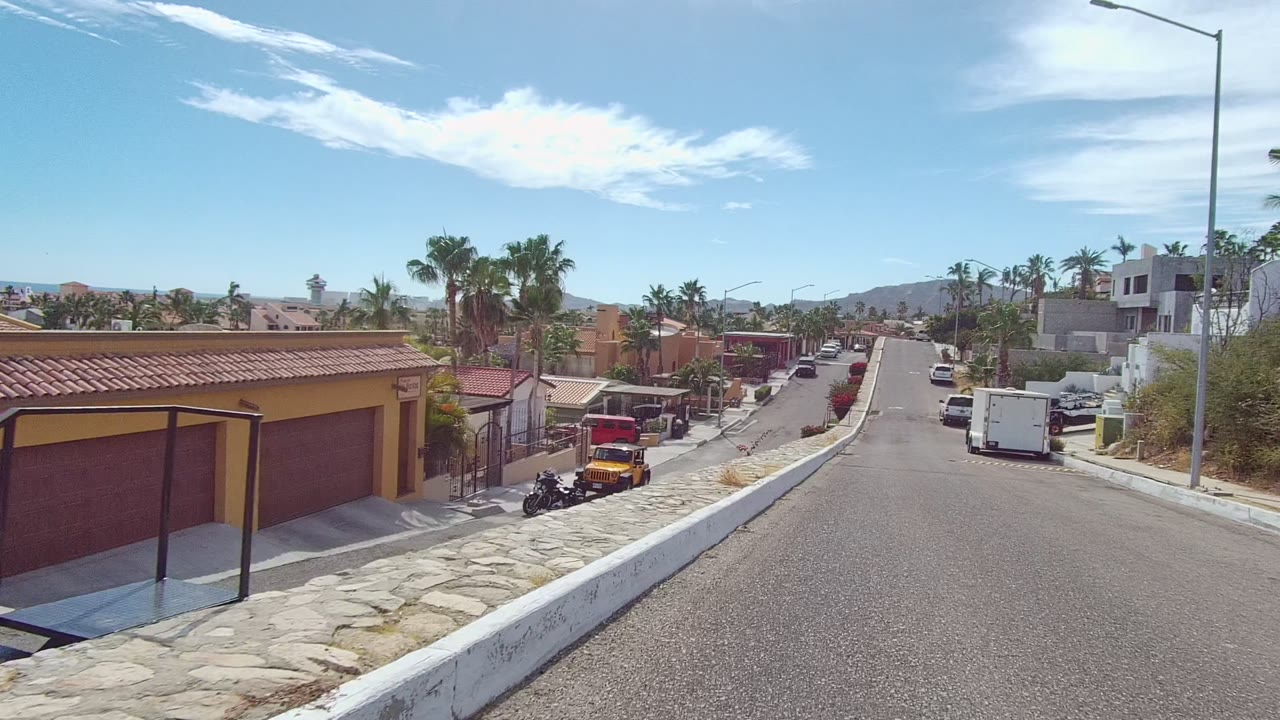 Forward road view past a yellow house, palm trees, and a yellow Jeep.