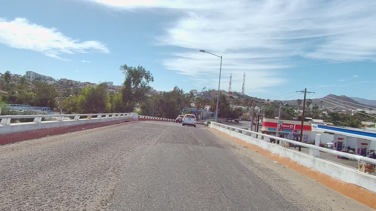 Vehicle-height view along a rough bridge road with cars and hills ahead