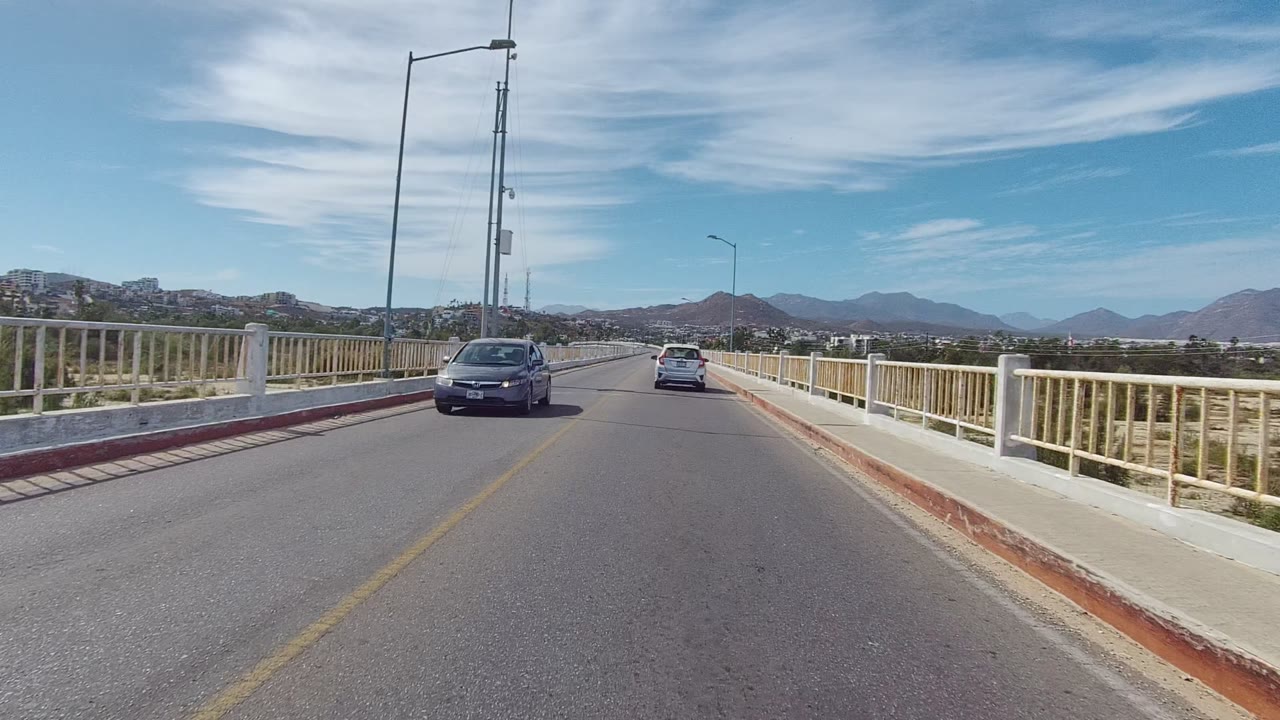 Oncoming car passes on a bridge road with mountains in the background.