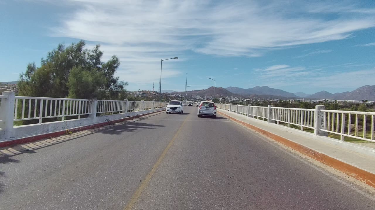 Two cars ahead on a bridge road bordered by white railings.