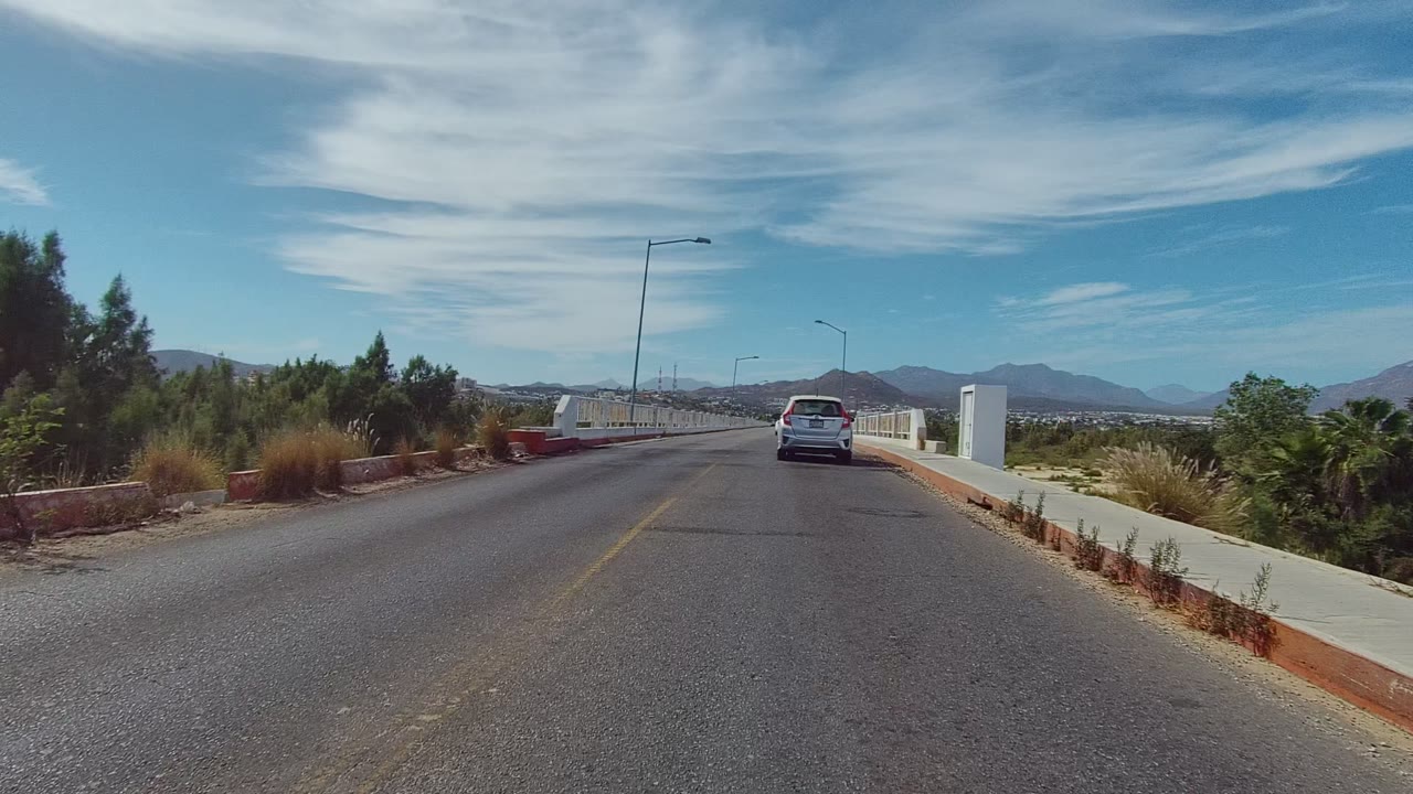 White sedan driving away on a paved road near bridge railings.