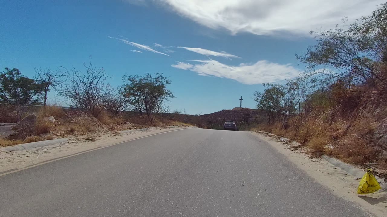 Curving paved road through arid brush with a car ahead