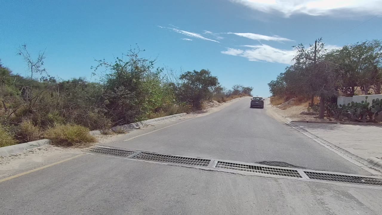 Car passes a paved road section with a drainage grate across the lane.