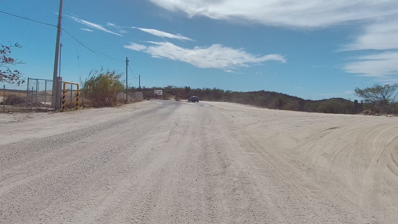 Roadside gravel curve with utility pole, rocks, scrub, and open sky.