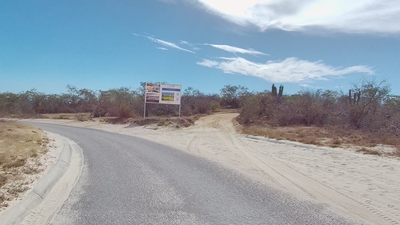 Road curve approaching a billboard beside dry brush