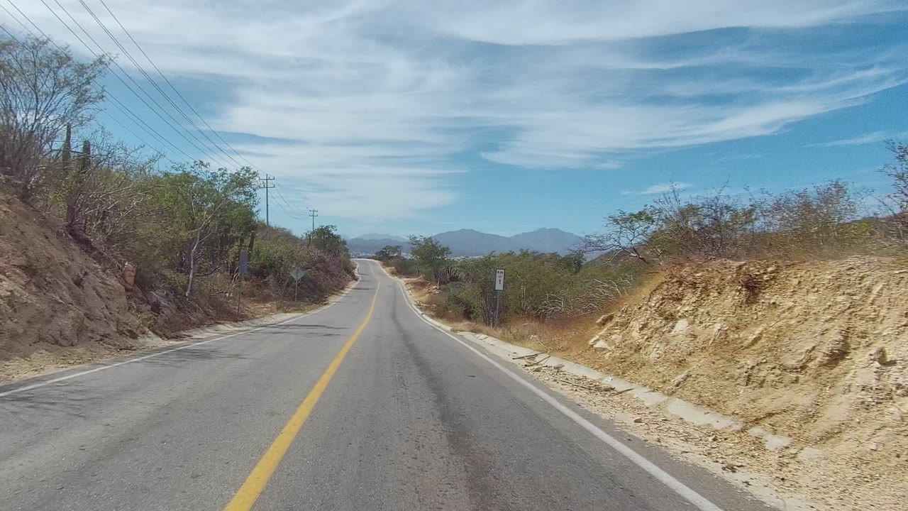 Curving asphalt road bordered by dry brush and utility lines