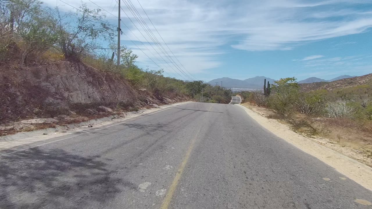 Road bend bordered by rocky desert brush and overhead utility lines