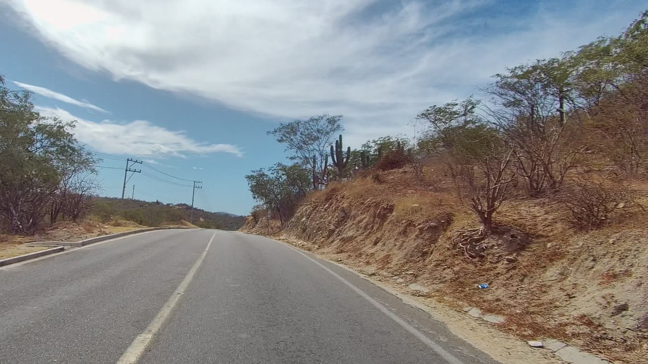 Paved road beside dry cut slope with power poles and scrub