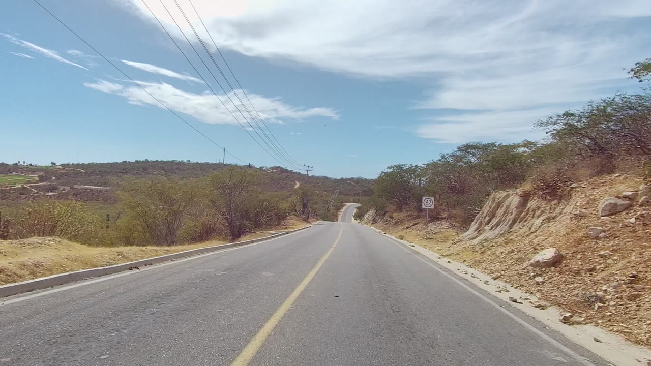 Rural road passing dry brush, utility wires, and a roadside sign