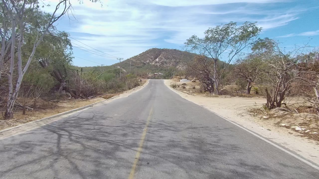 Road through dry brush with a hill ahead and utility lines above.