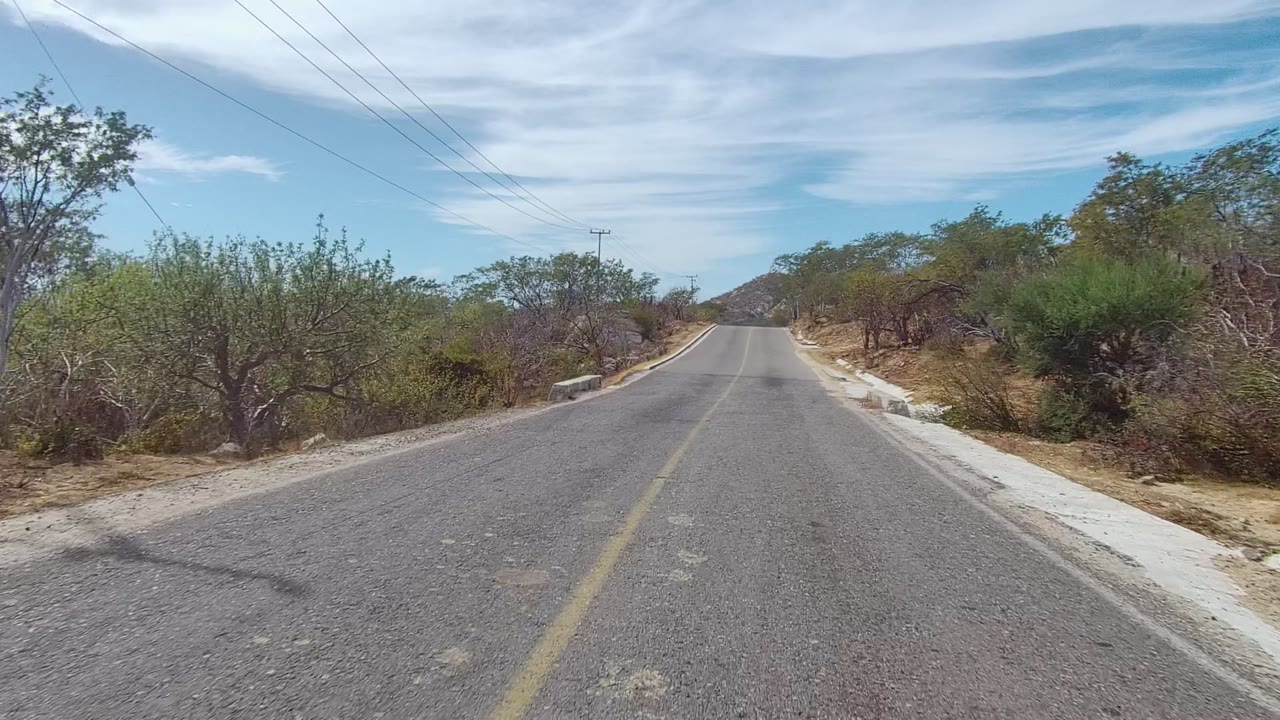 Rural asphalt road with scrubland and low hills ahead