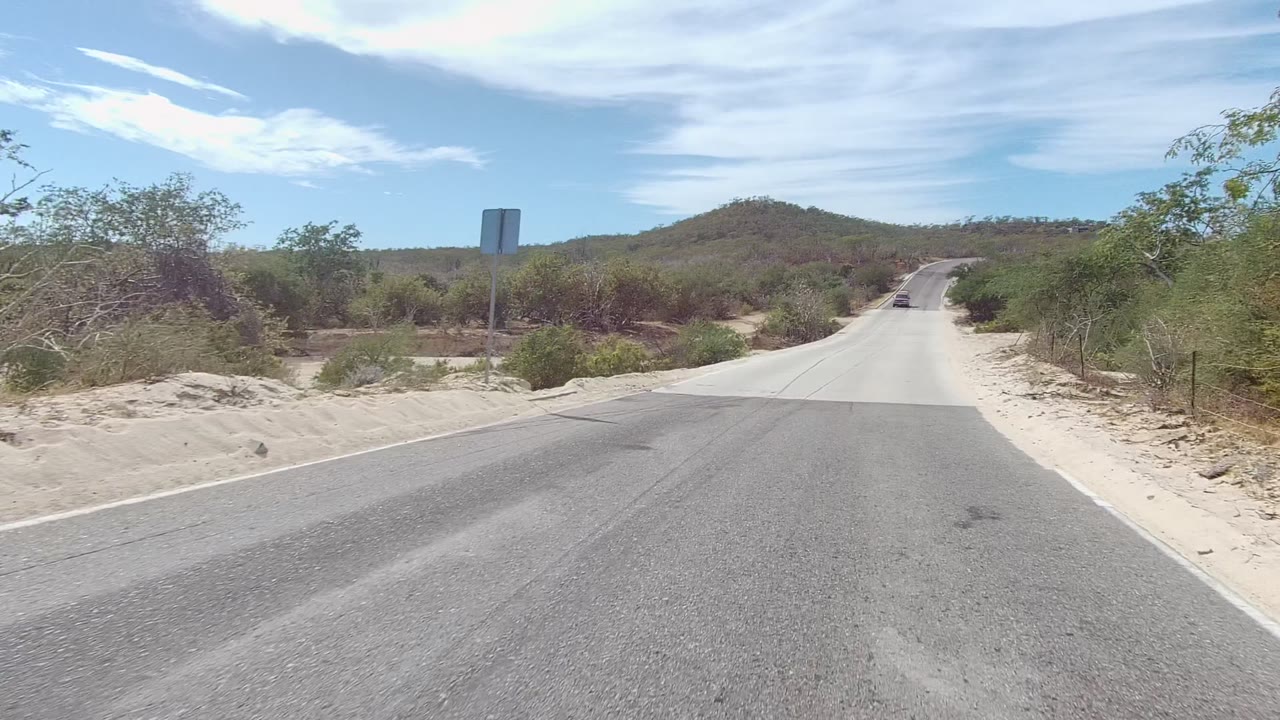 Straight paved road leading toward low desert hills