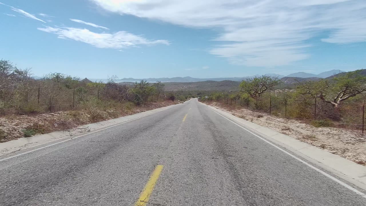 Centered road view with dry vegetation and mountains ahead.
