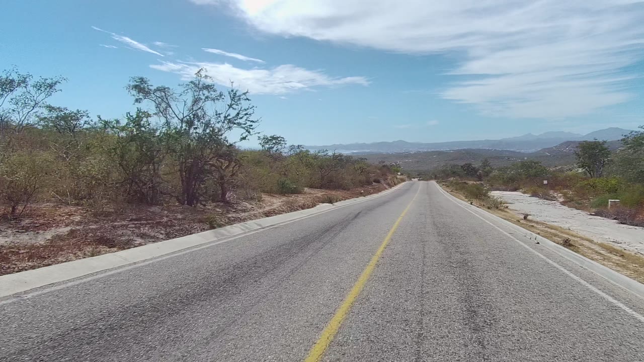 Centered road view with scrubland shoulders and high white clouds