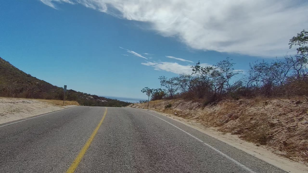 Road curving between sandy shoulders and sparse brush.