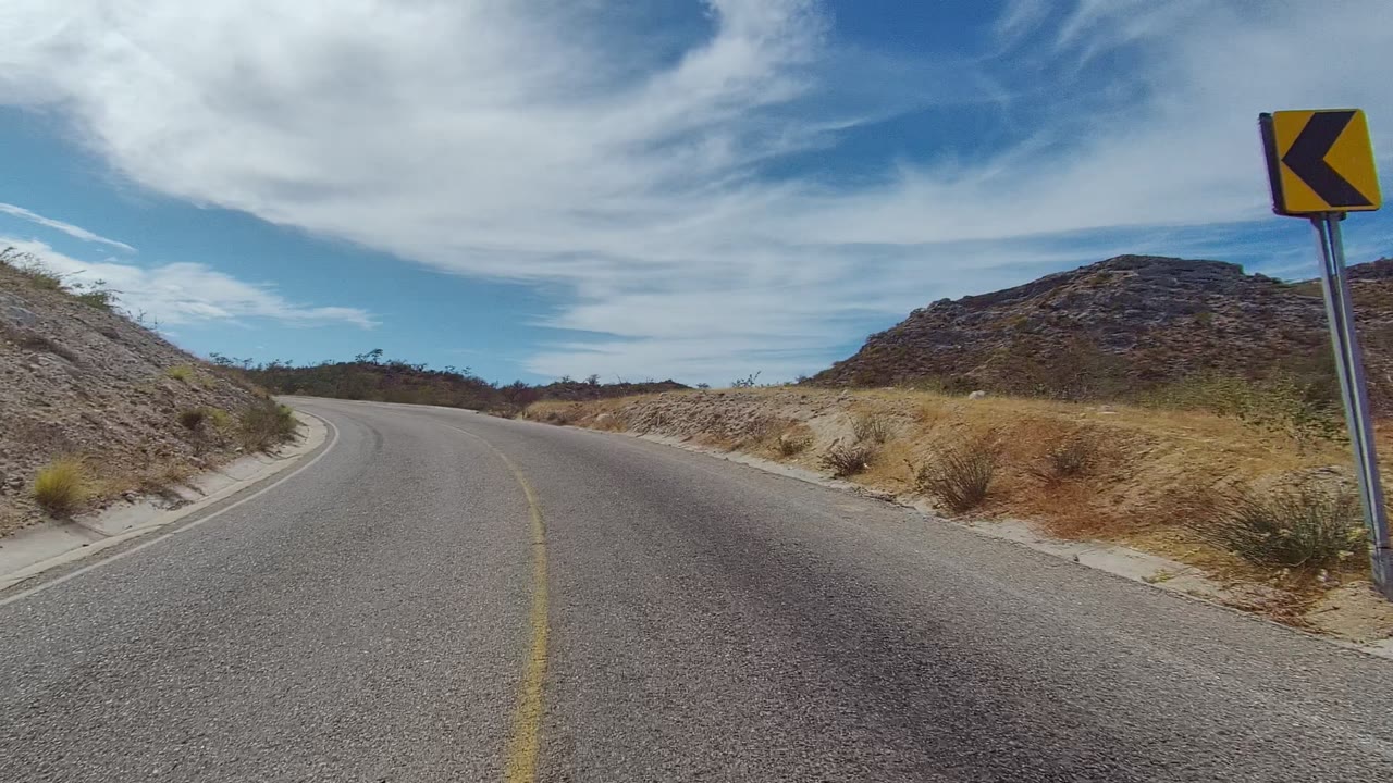Road bend passing a yellow curve sign beside dry brush.