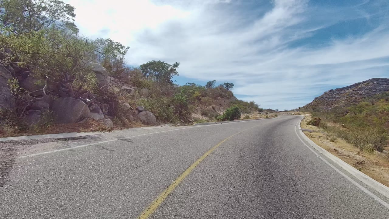 Road bend passing rocks, shrubs, and low arid hills