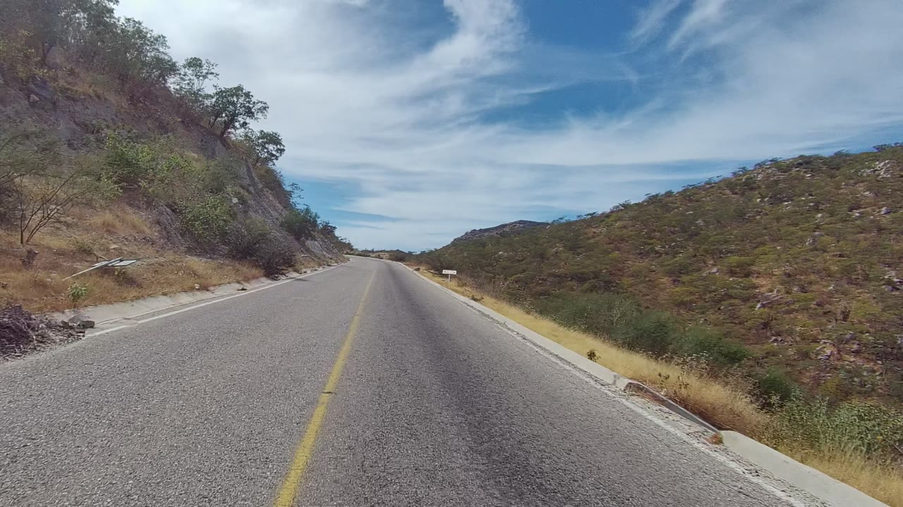 Empty paved road with yellow line beside scrubby hillsides.
