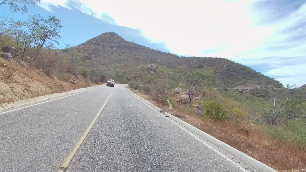 Car closer on a curved road below a rounded hill