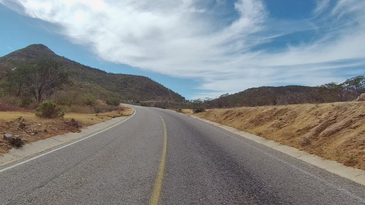 Road bending right with brushy hillside and dry shoulder.