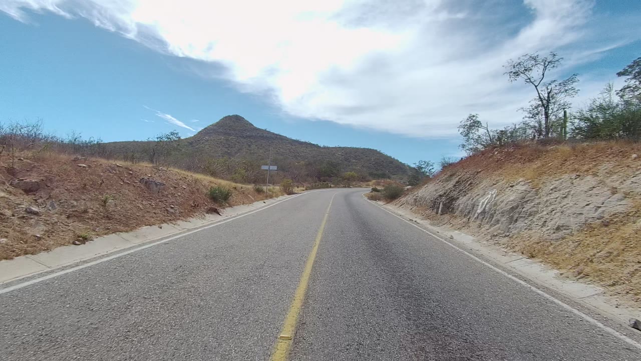 Curving paved road with dry roadside cut and hill ahead