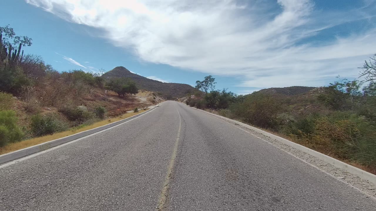 Road curving gently through arid roadside brush and rocky hills
