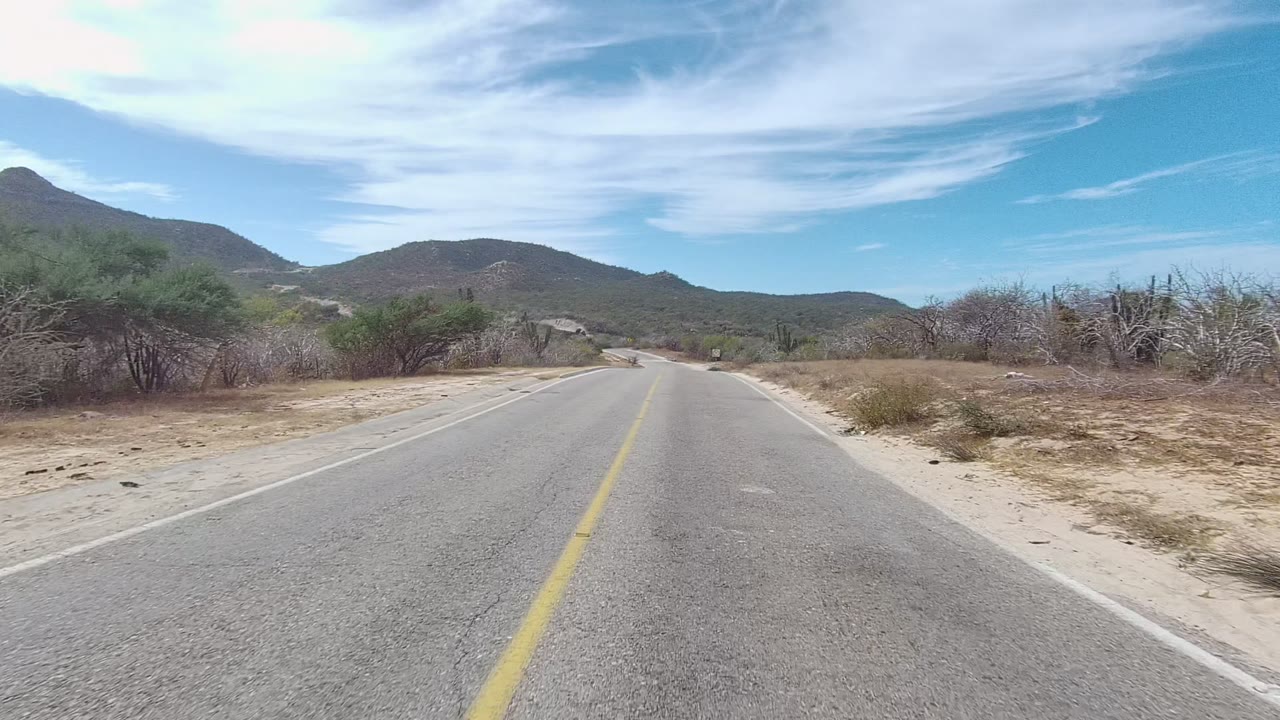 Curving paved road bordered by dry brush and desert hills