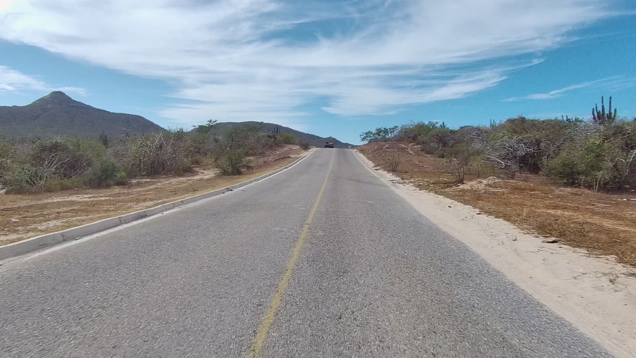 Desert road with a small dark vehicle far ahead near the horizon.