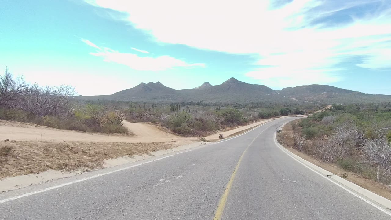 Desert road with sandy roadside paths and low mountains ahead.