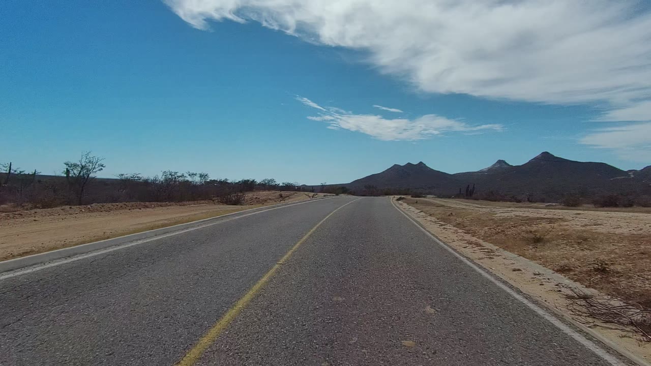 Straight desert highway with scrubland and mountains ahead.