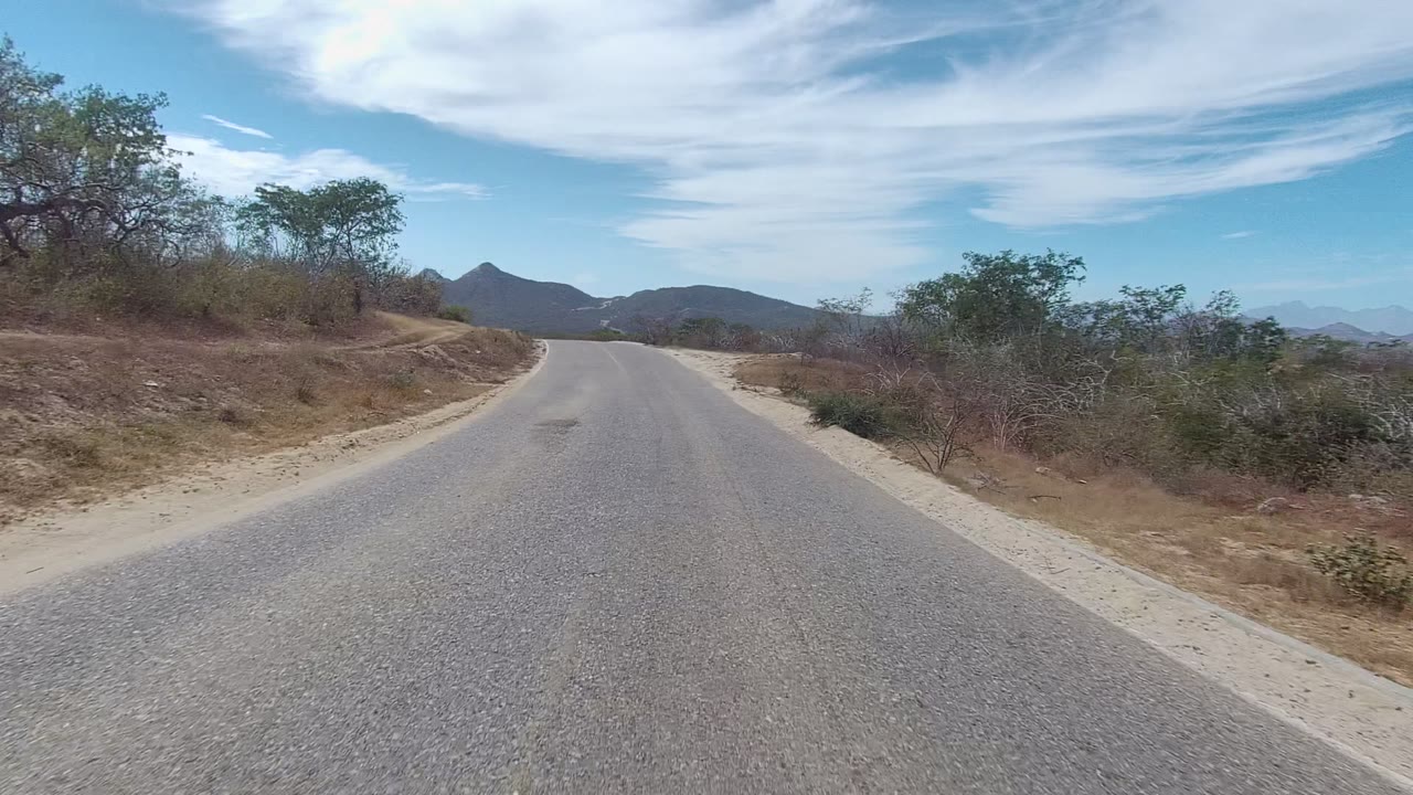 Empty paved road with dry shrubs and mountains in the distance