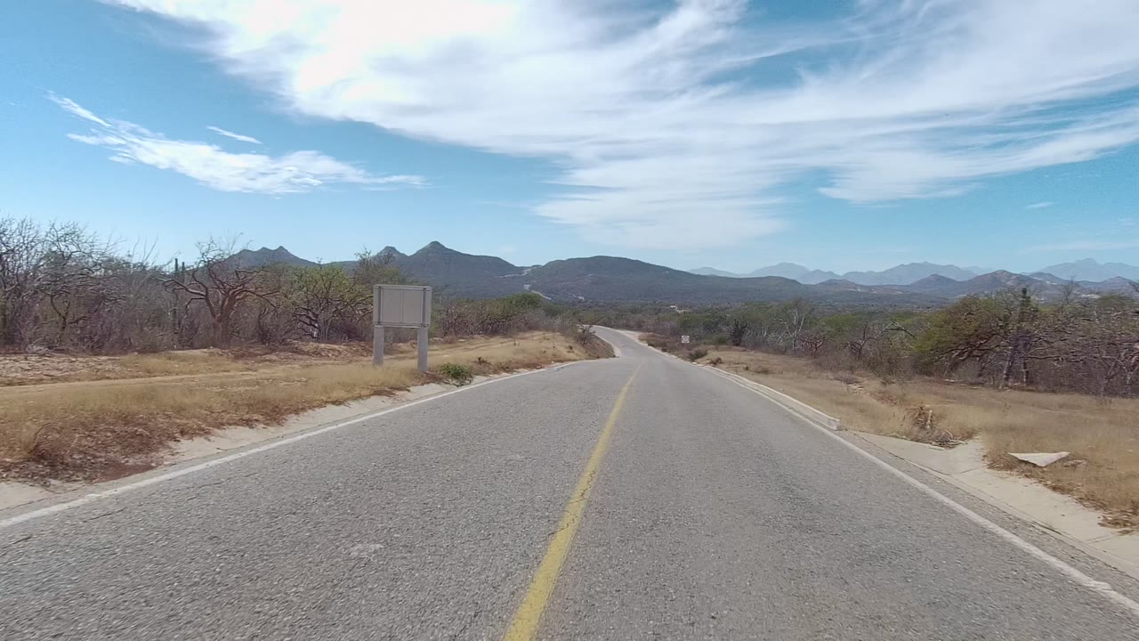 Road entering arid terrain with roadside sign and mountain horizon